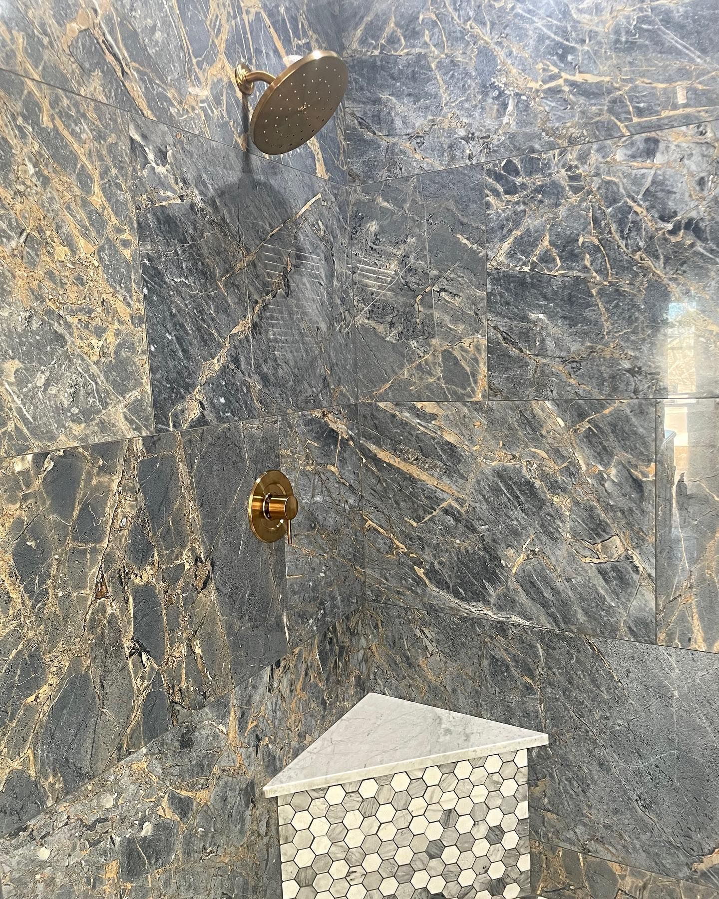Shower with gold fixtures and dark gray marble tile, corner shelf.
