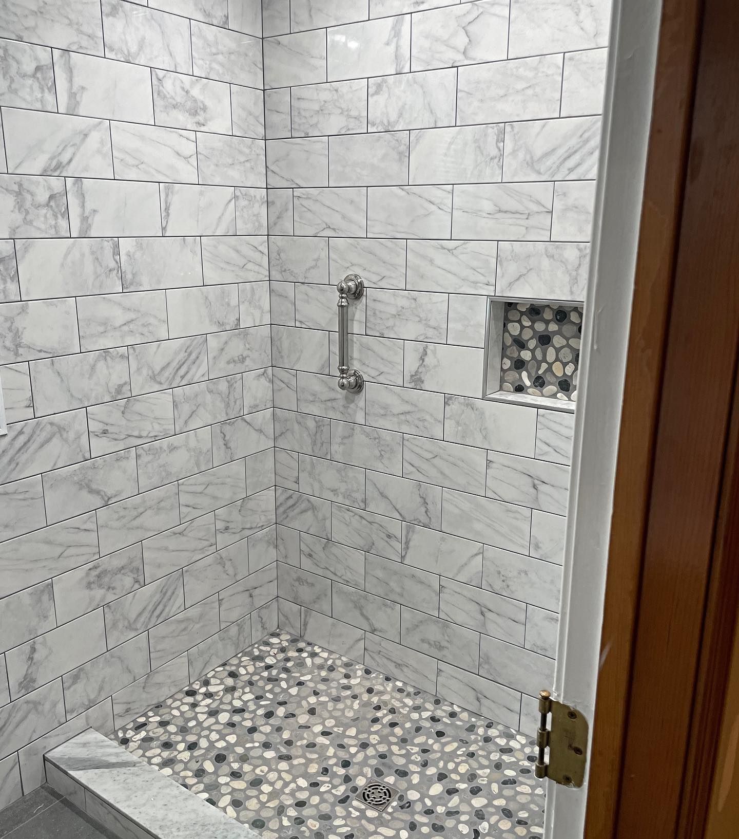 Shower stall with white and gray tiled walls and floor, and stone pebble floor.