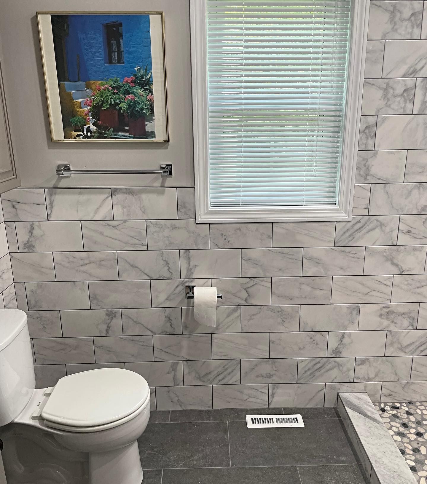 Bathroom with white and gray marble tile walls, white toilet, and window with blinds.