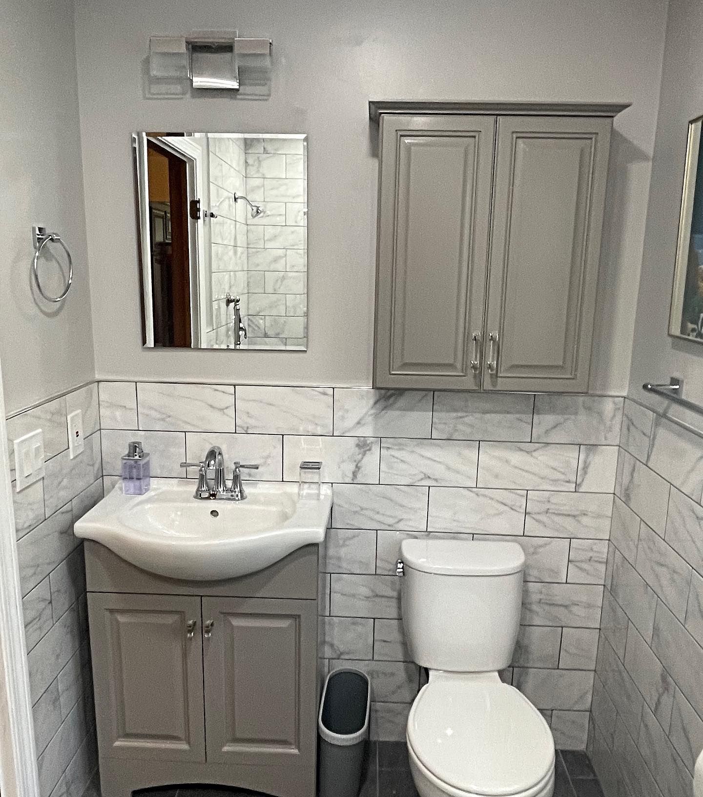 Bathroom with marble-look tile, gray cabinets, sink, toilet, mirror, and a wall-mounted towel ring.