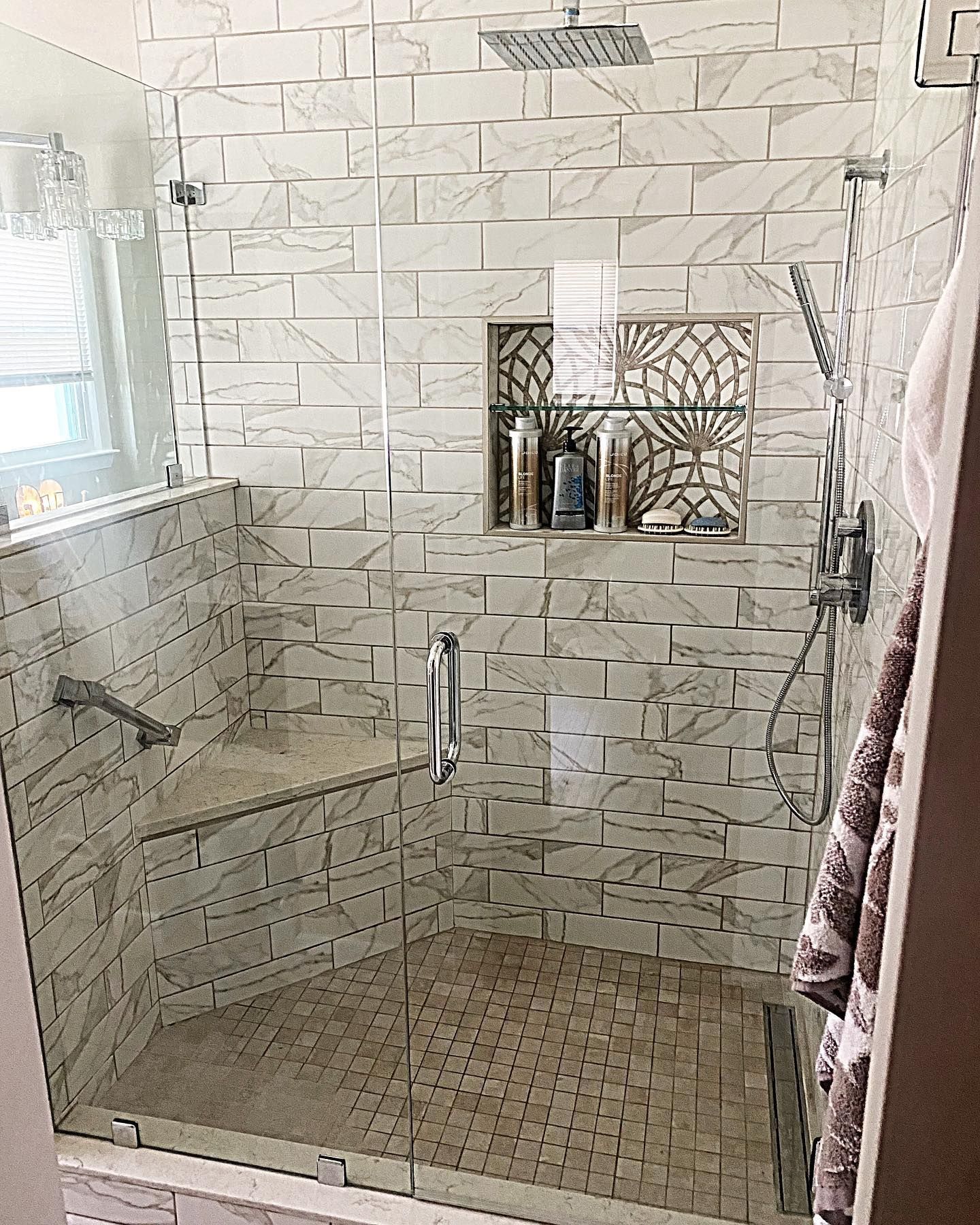 Glass-enclosed shower with white textured tile walls, built-in shelf, and decorative niche. Showerhead and handheld sprayer visible.