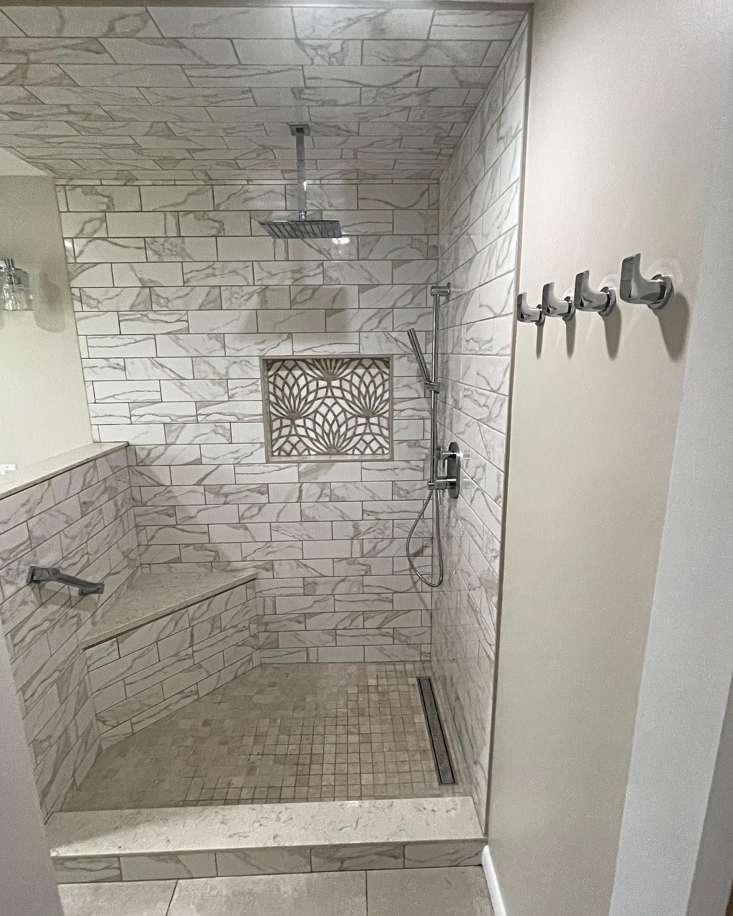 Tile shower with a built-in bench, rain shower head, and decorative niche. Gray and white color scheme.