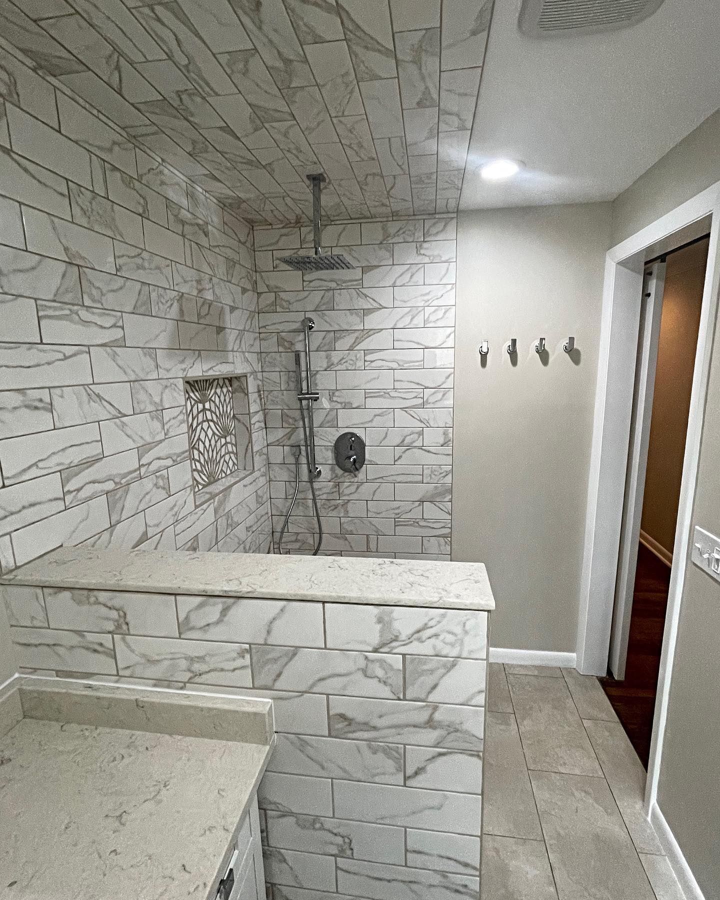 Modern bathroom with tiled shower, countertop, and doorway.