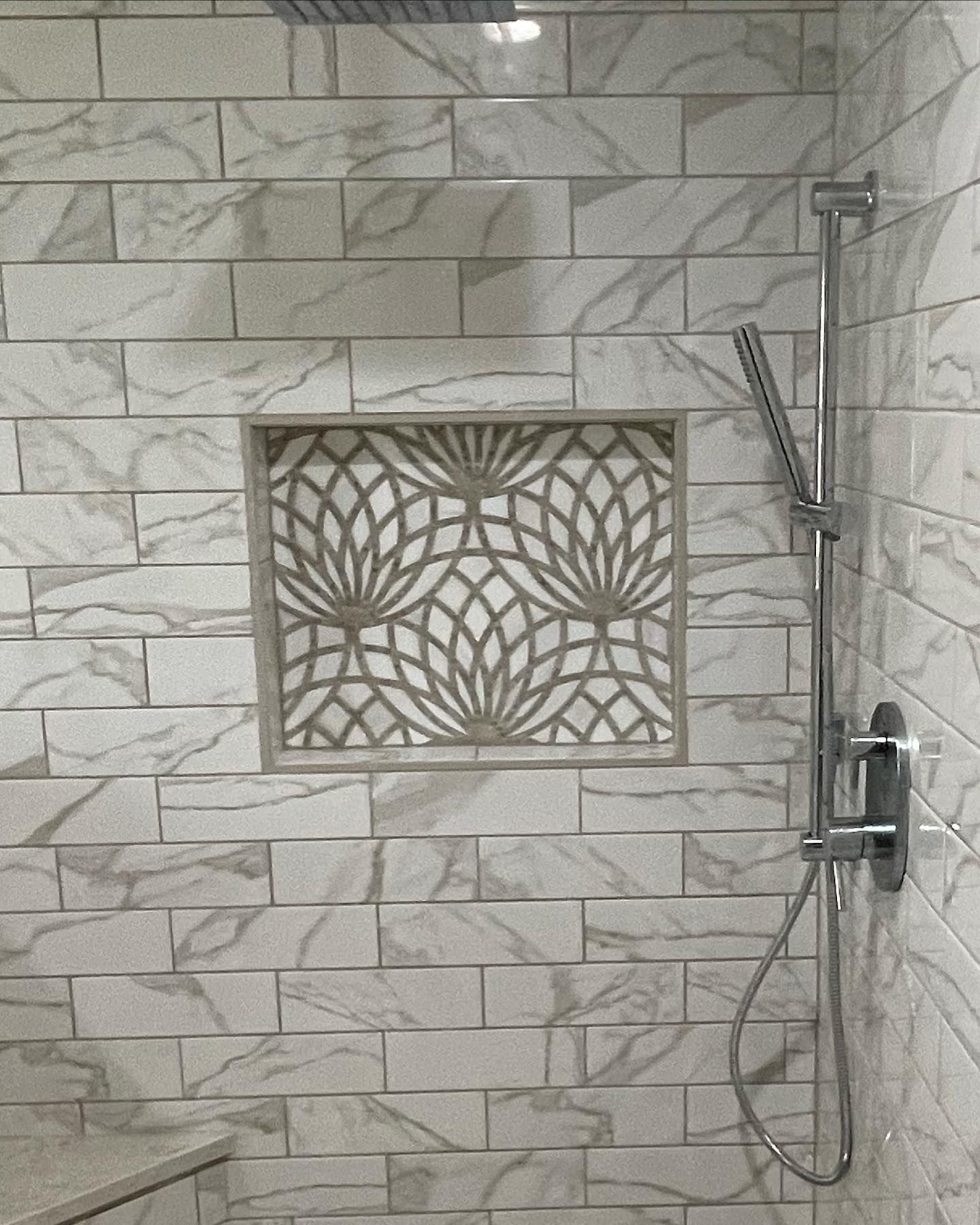 Shower with white and gray tile, decorative niche, and silver shower fixtures.
