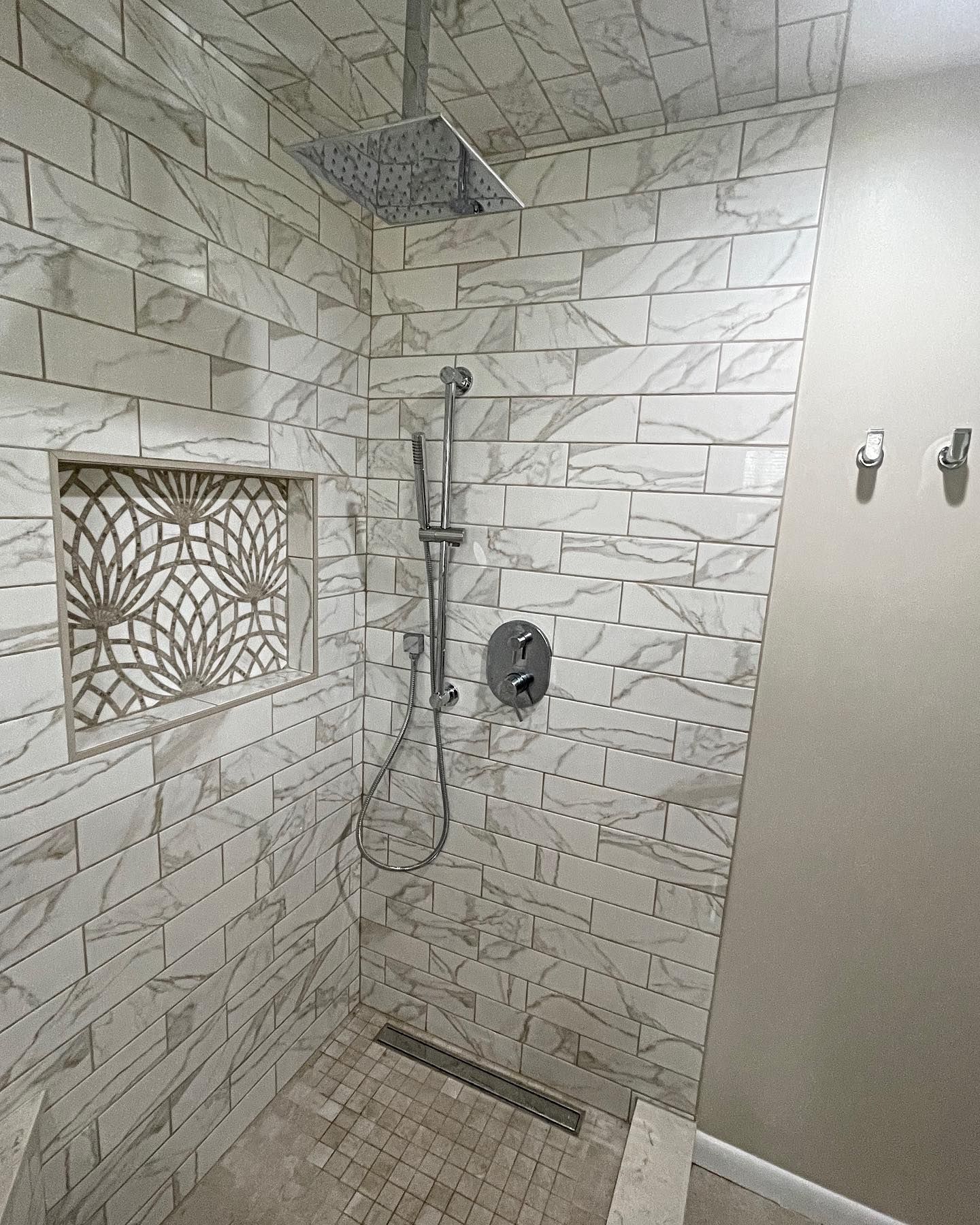 Modern shower with rectangular tiles and decorative niche. Silver fixtures.
