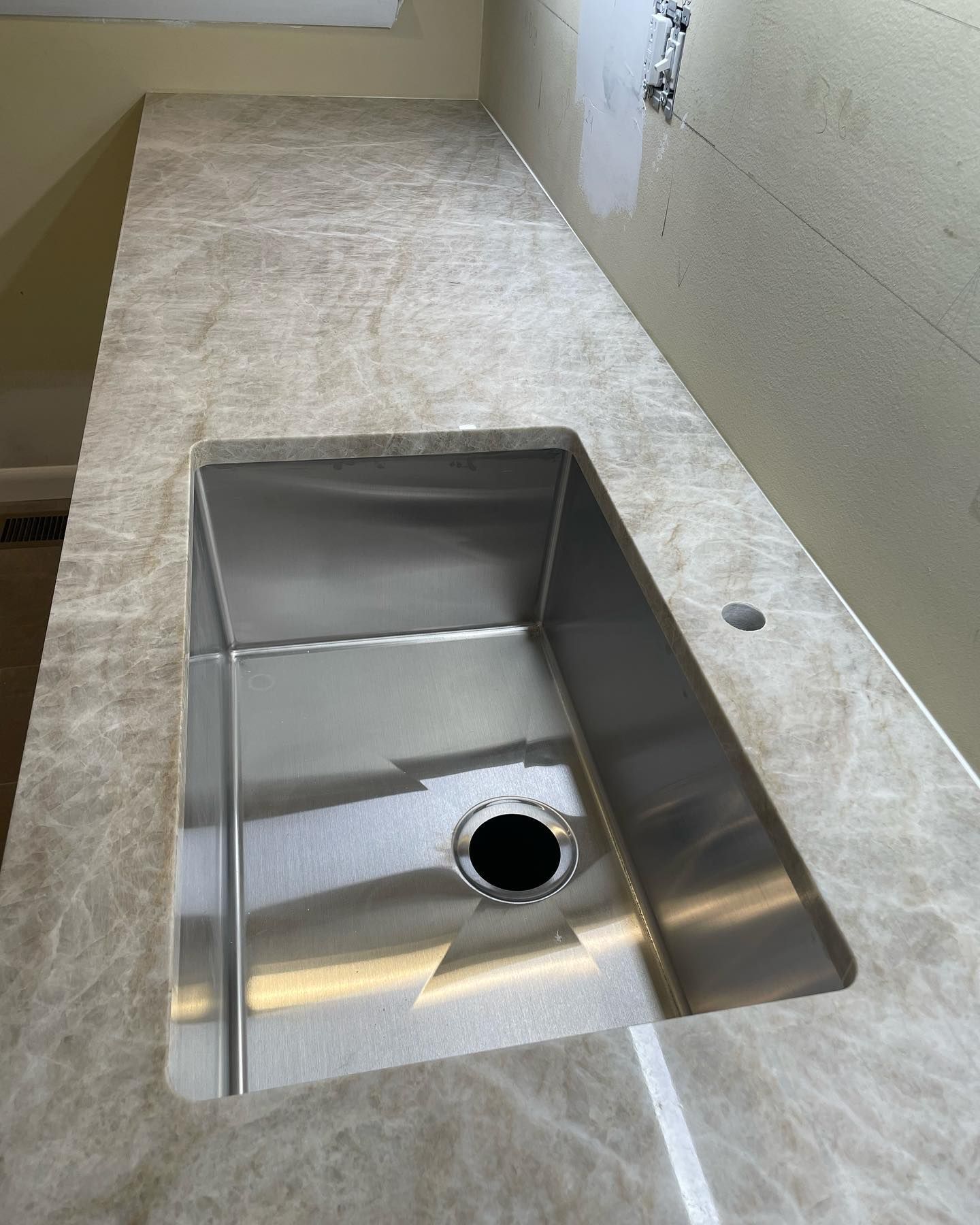 Stainless steel sink installed in a light brown countertop with a hole for a faucet.