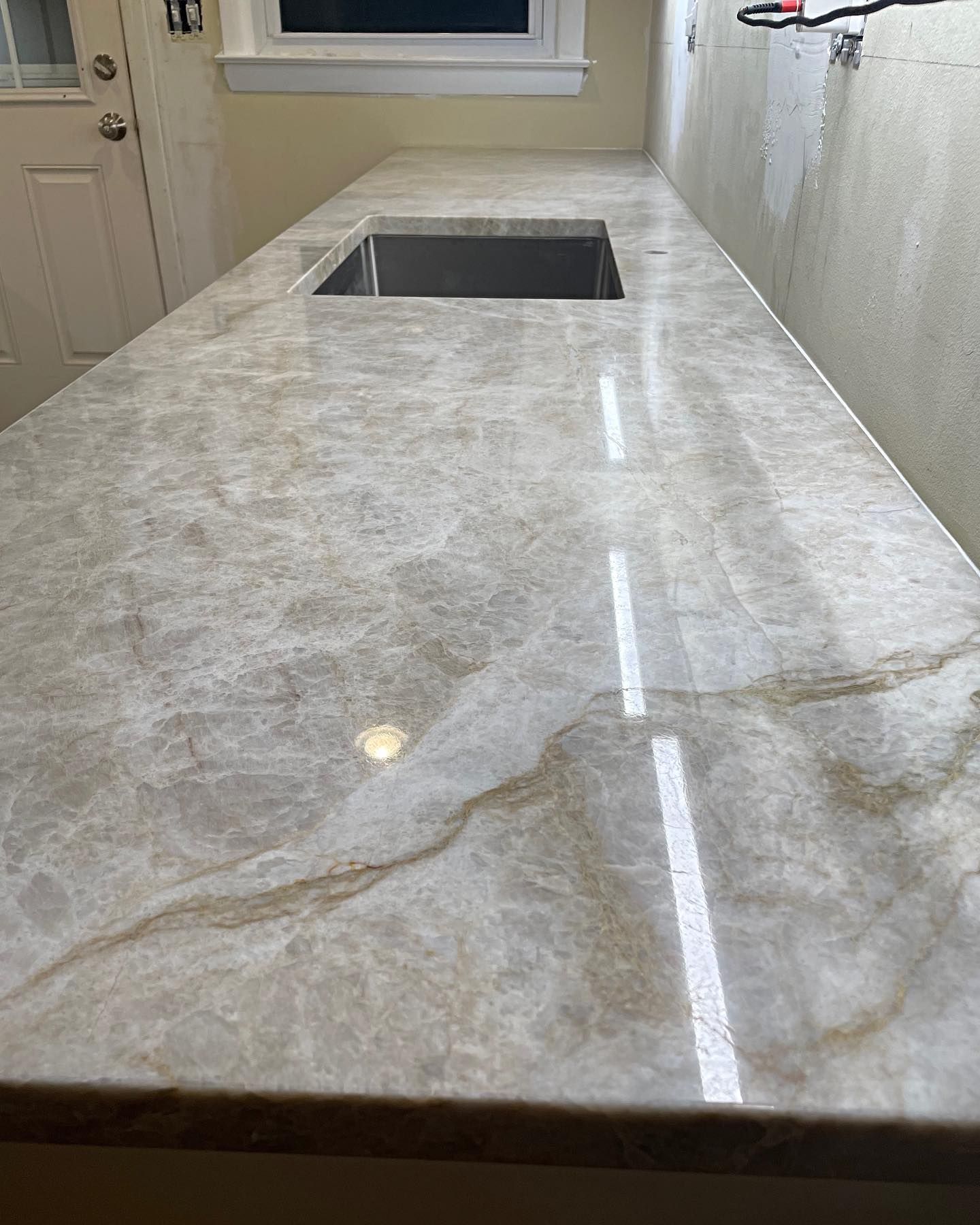 Light-colored countertop with marble-like pattern and a stainless steel sink, in a kitchen setting.