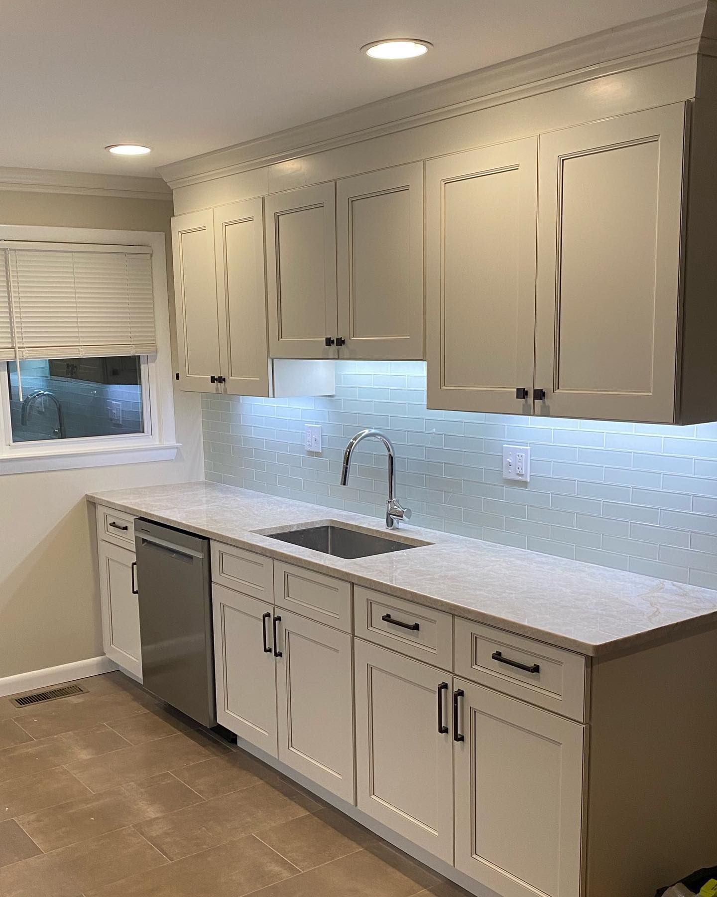 White kitchen with upper and lower cabinets, stainless steel appliances, and a window.