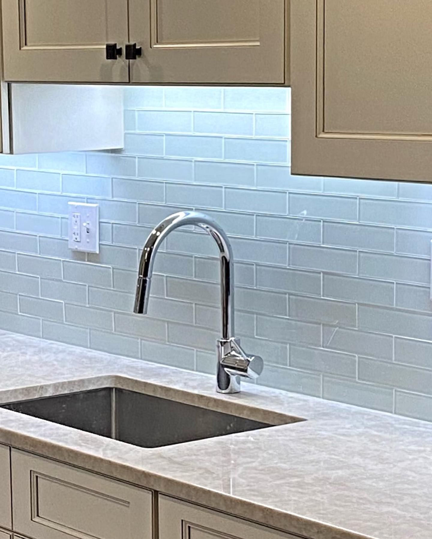 Kitchen sink with a chrome faucet, light blue tile backsplash, and cream-colored cabinets.