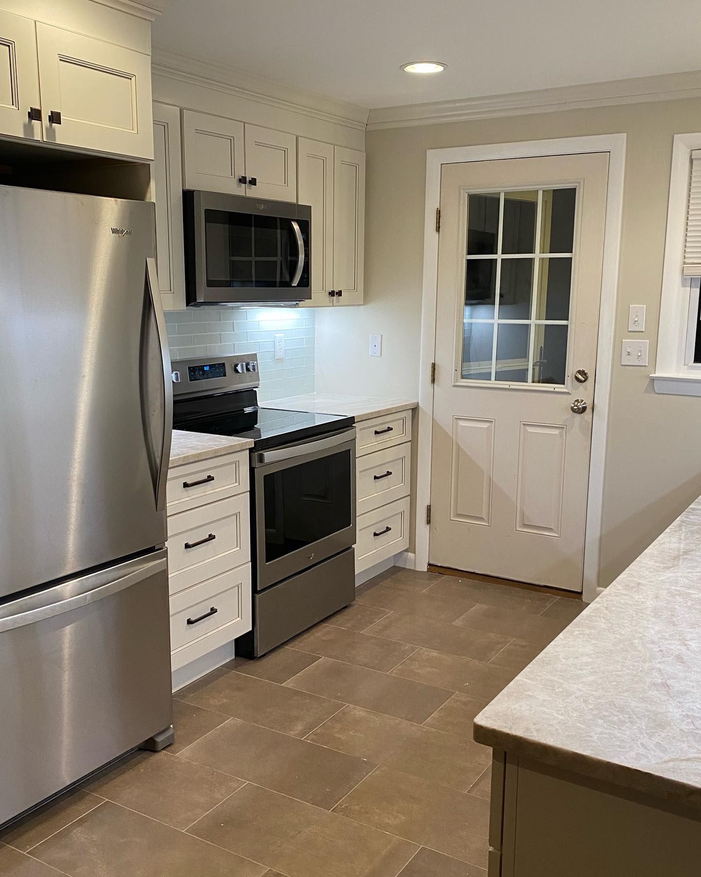 Stainless steel kitchen with white cabinets, oven, microwave, and a door.