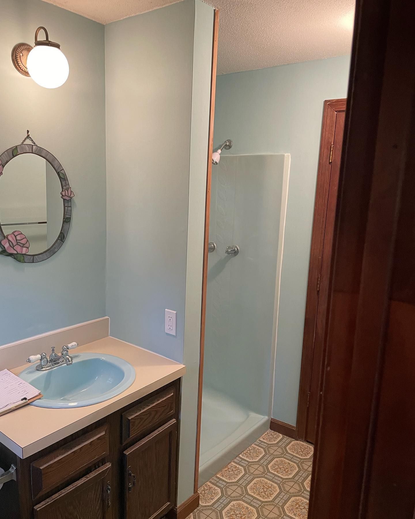 Bathroom with light blue walls, vanity, shower, and patterned floor.