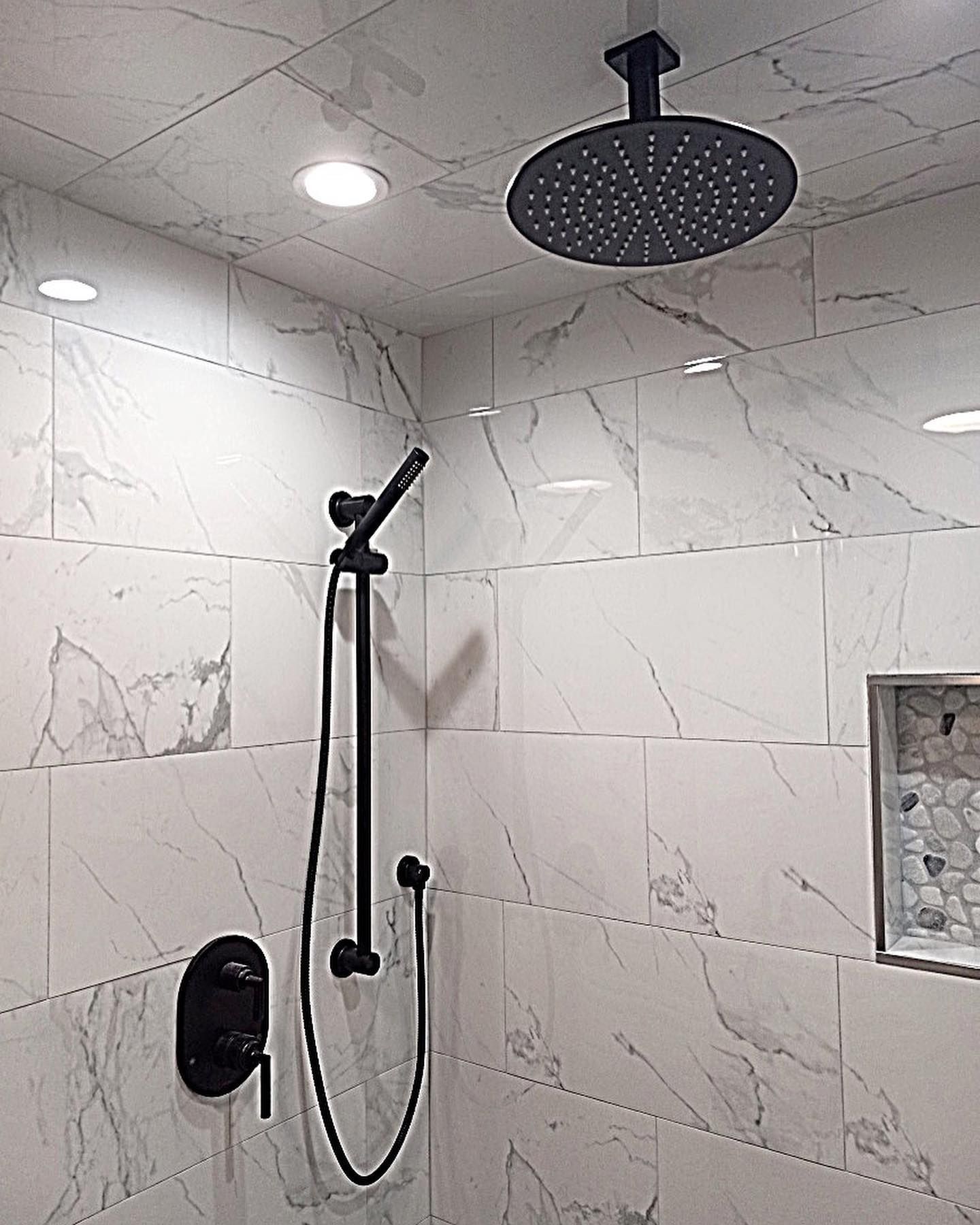 Bathroom with white marble-look tiles, black shower fixtures, and a recessed shelf.
