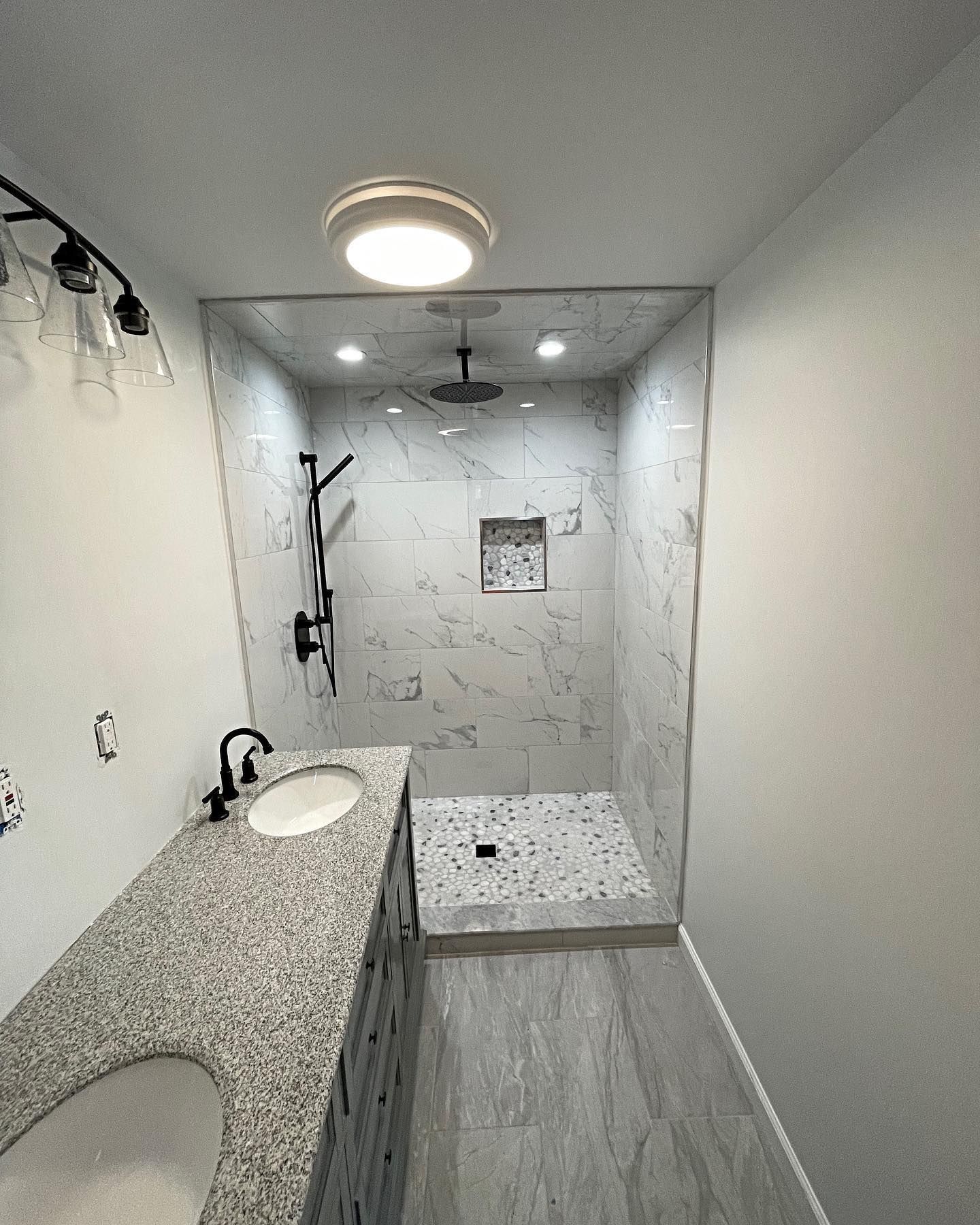 Bathroom with shower: gray marble tiles, black fixtures, granite countertop, round ceiling light.