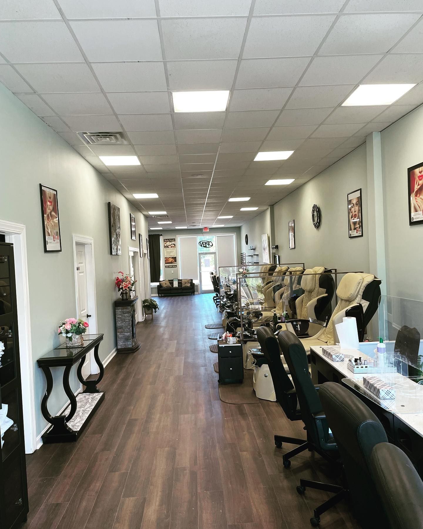 Long, narrow nail salon interior with manicure stations, artwork, and brown wood floors.