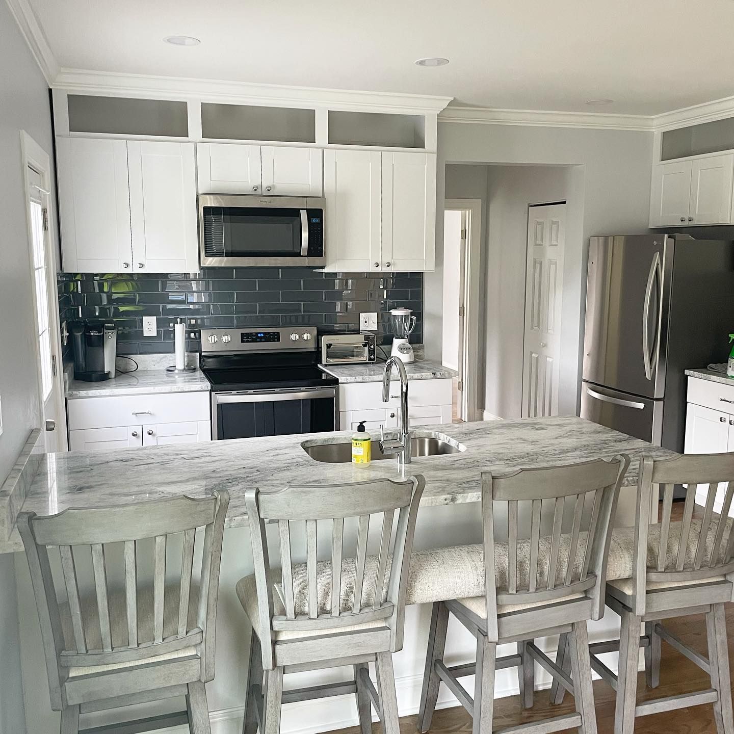 White kitchen with gray countertops and backsplash; bar stools at the island.