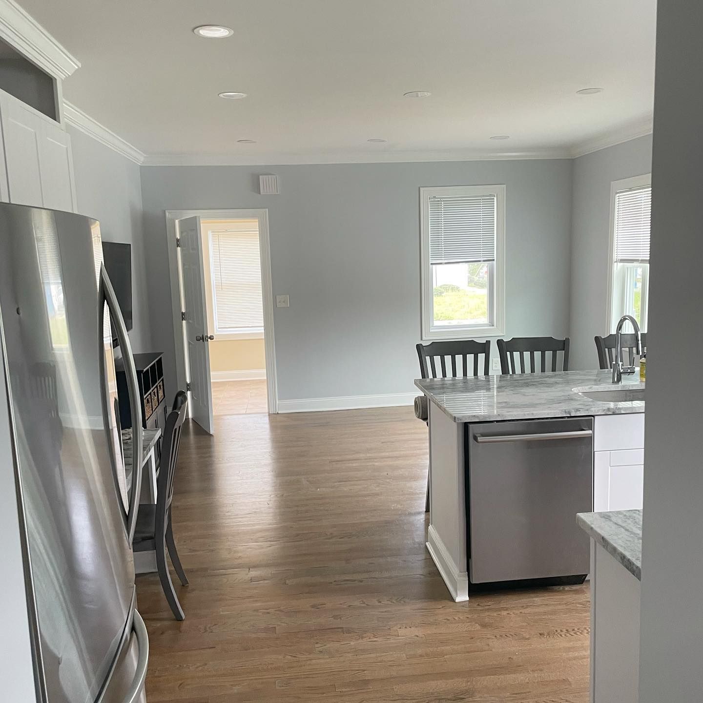Kitchen with wood floors, island, cabinets, and stainless steel appliances; open to living area with door and windows.