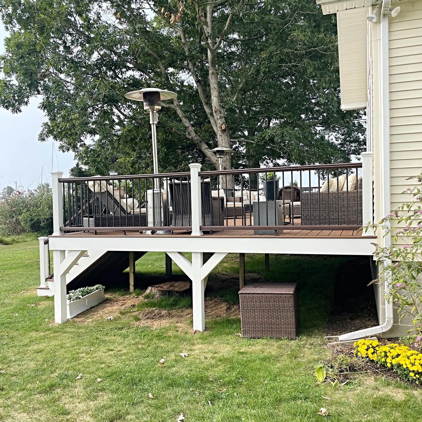 Deck with outdoor furniture, heater, and a large tree in the background. White deck with brown railings.