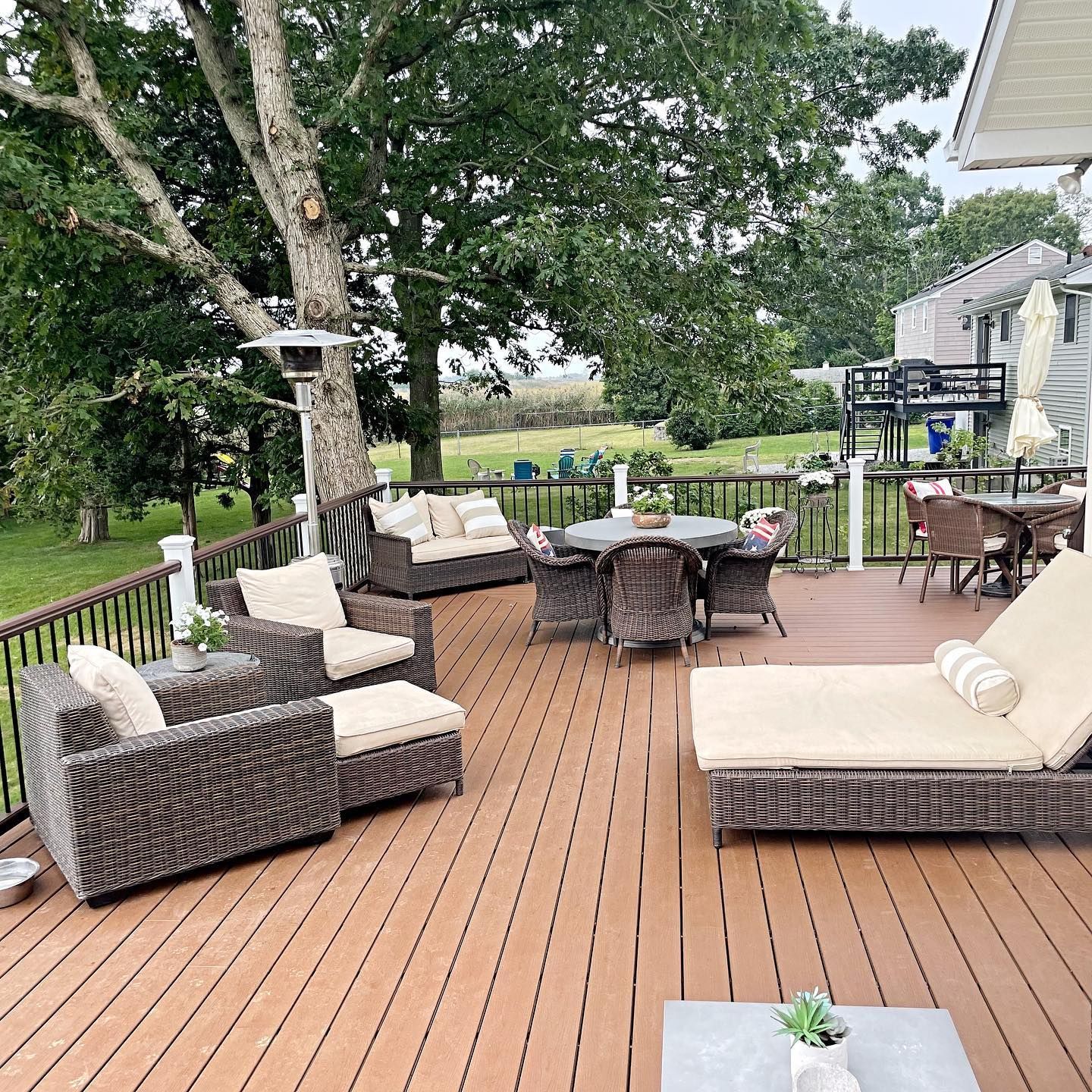 Outdoor deck with wicker furniture and a dining table, overlooking a grassy yard with trees.