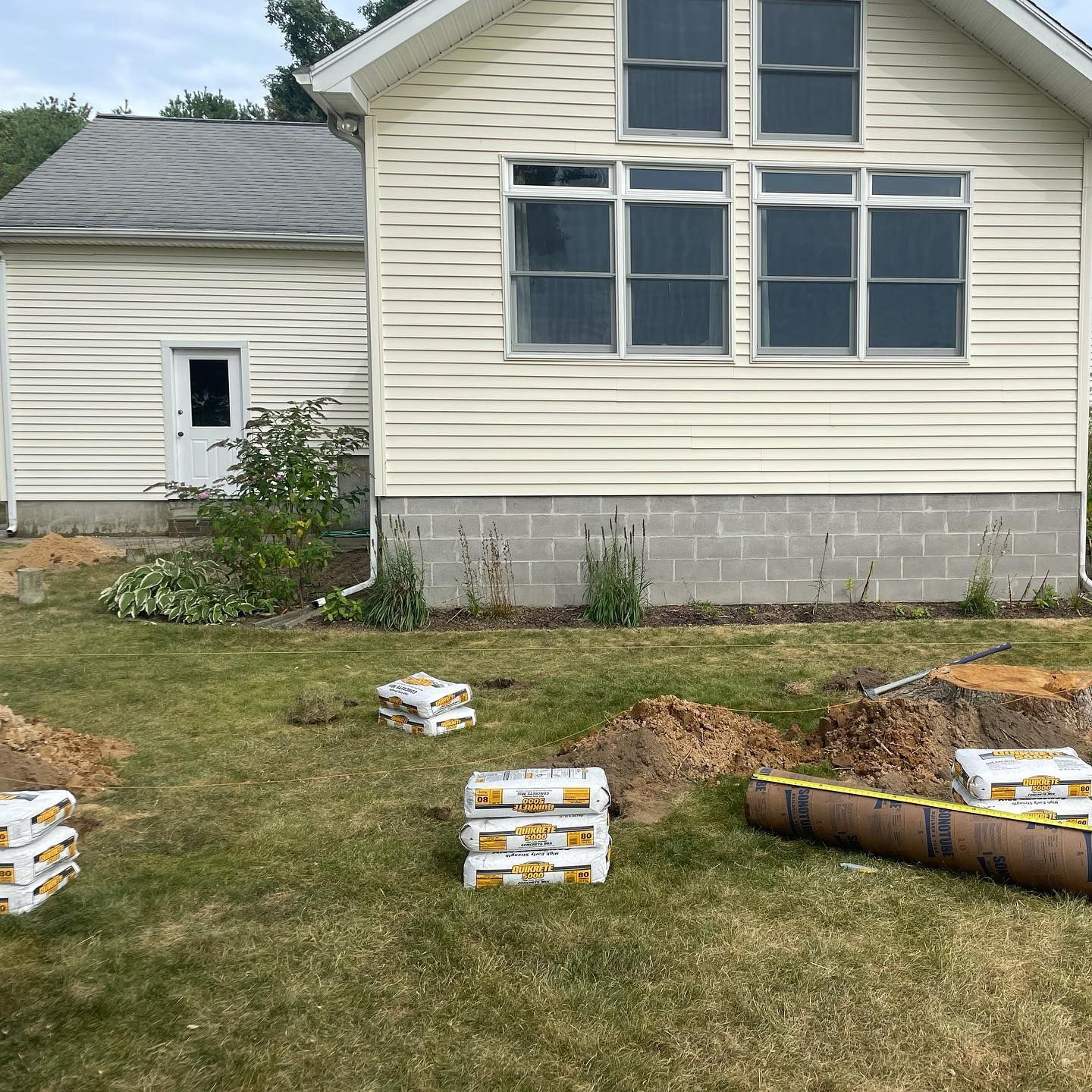 House with stacked concrete blocks in a yard, construction preparations underway.