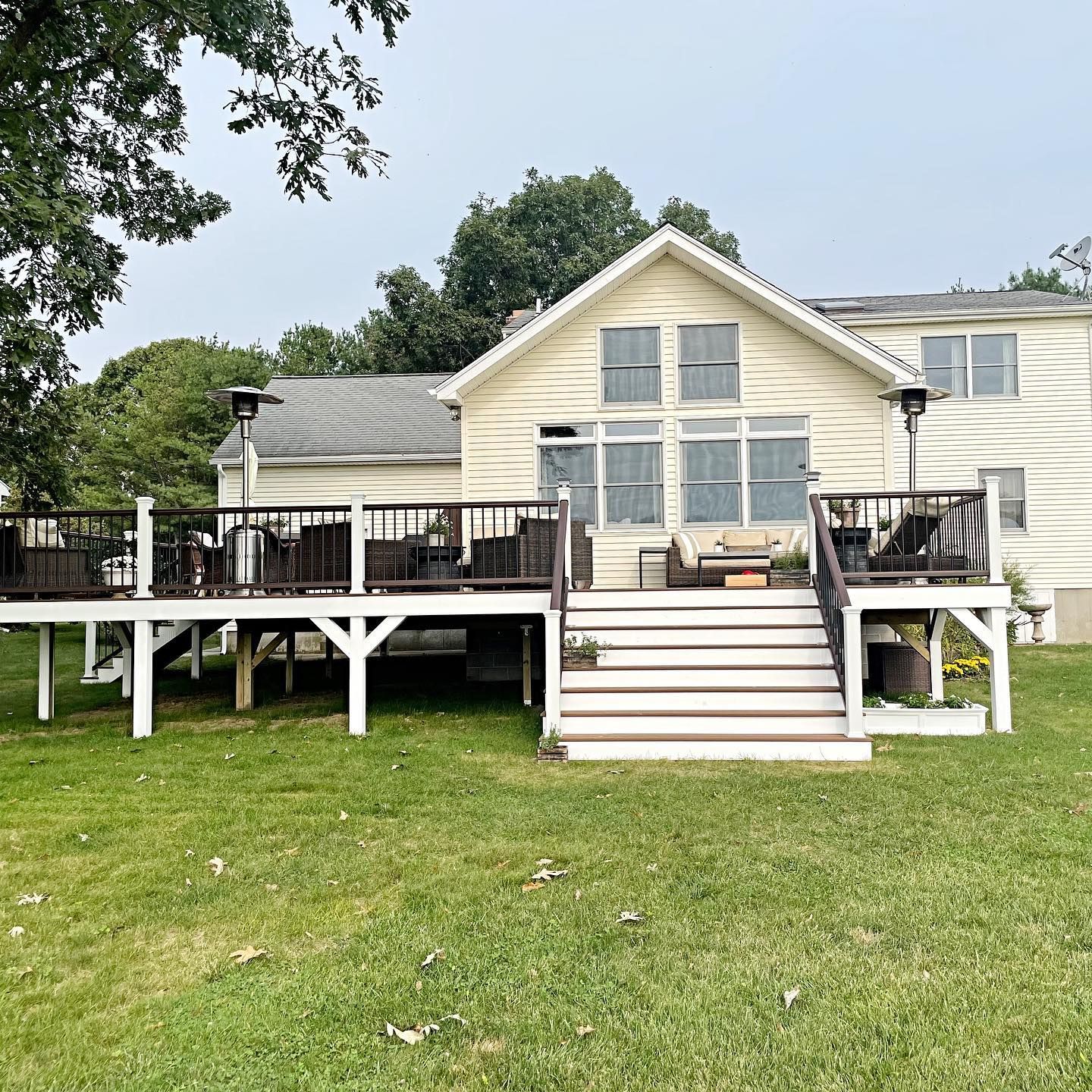 Beige house with a large wooden deck and green grass.