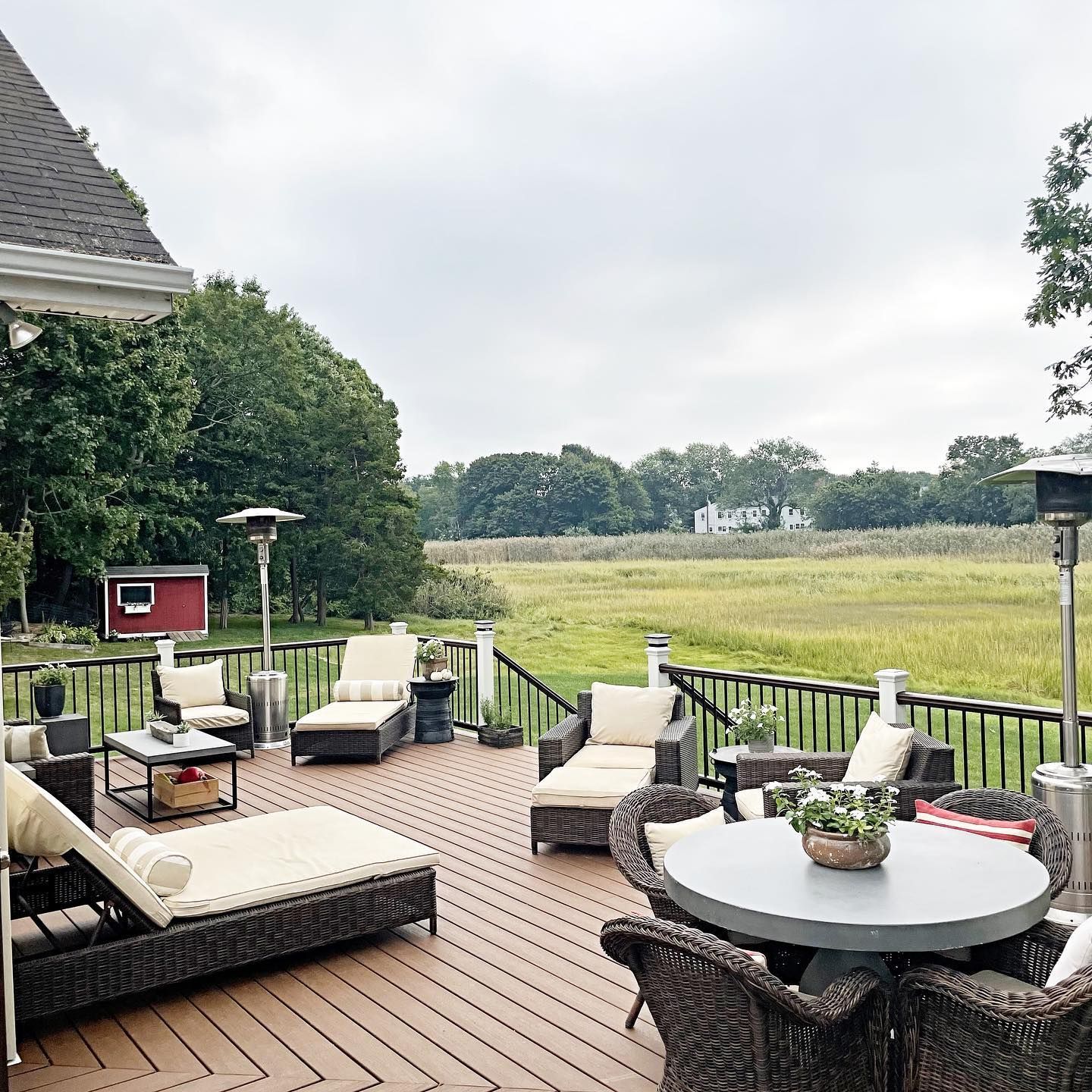 Outdoor deck with lounge chairs and table overlooking a field on a cloudy day.