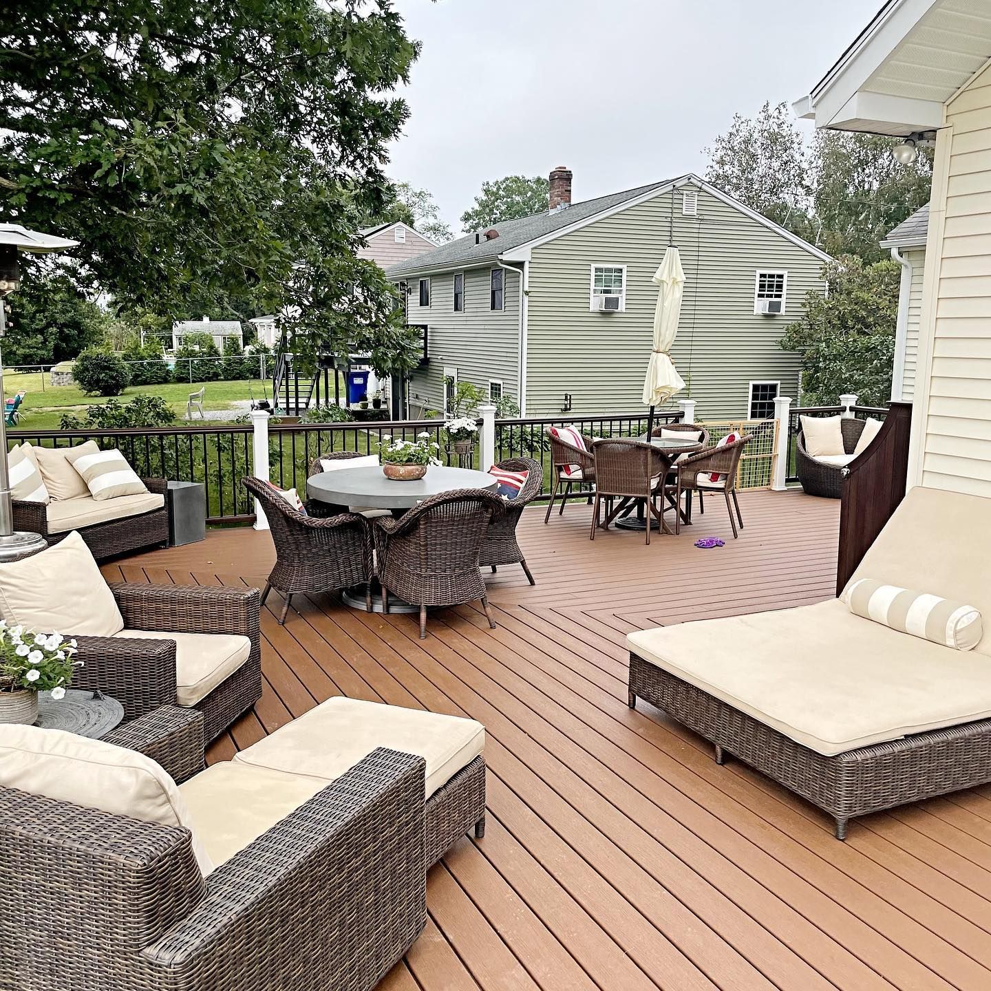 Deck with outdoor furniture: seating, dining set, and lounge chairs. Beige cushions, brown wicker, and neutral deck.