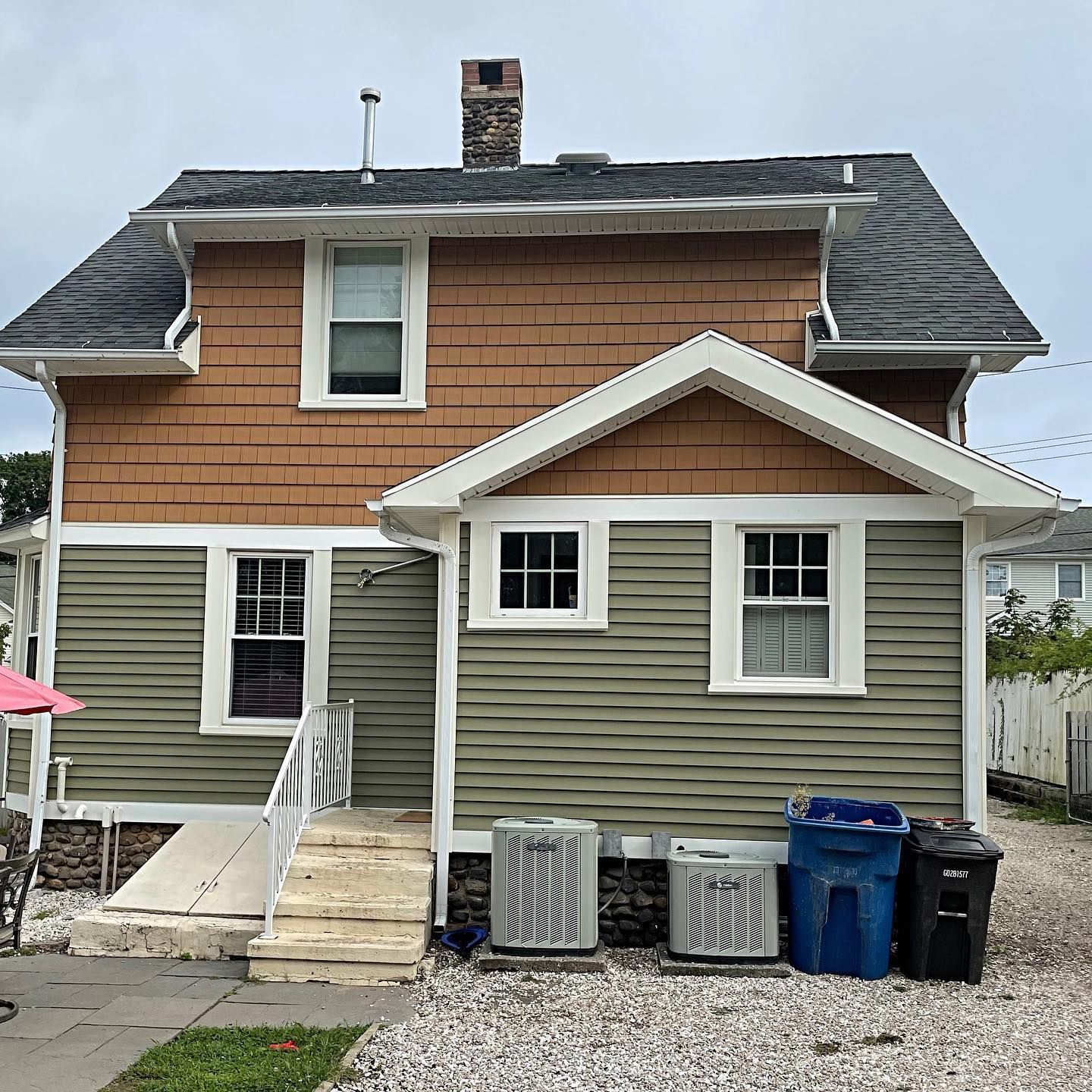 Back of a house with green and brown siding, steps, and two air conditioning units.
