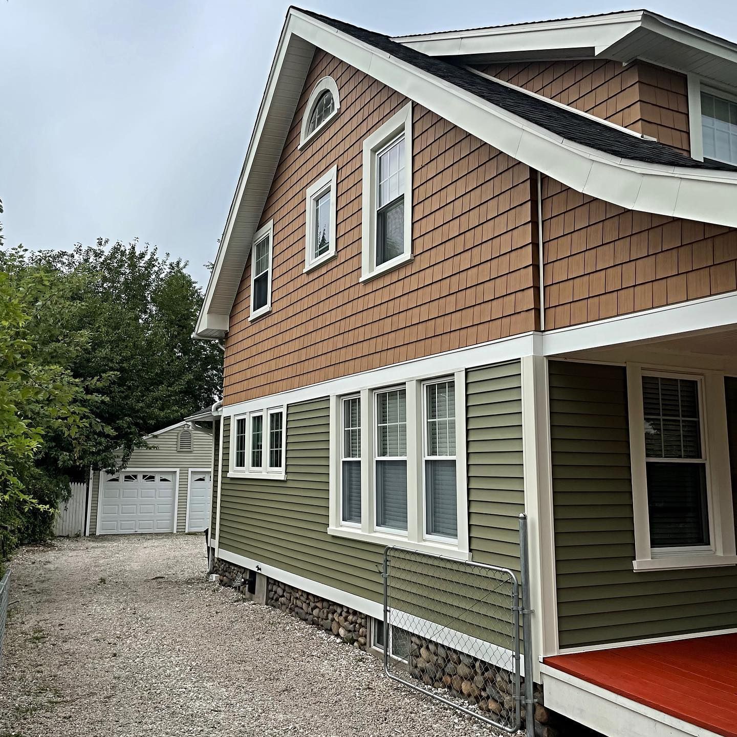 Two-story house with green and brown siding, white trim, and a gravel driveway.