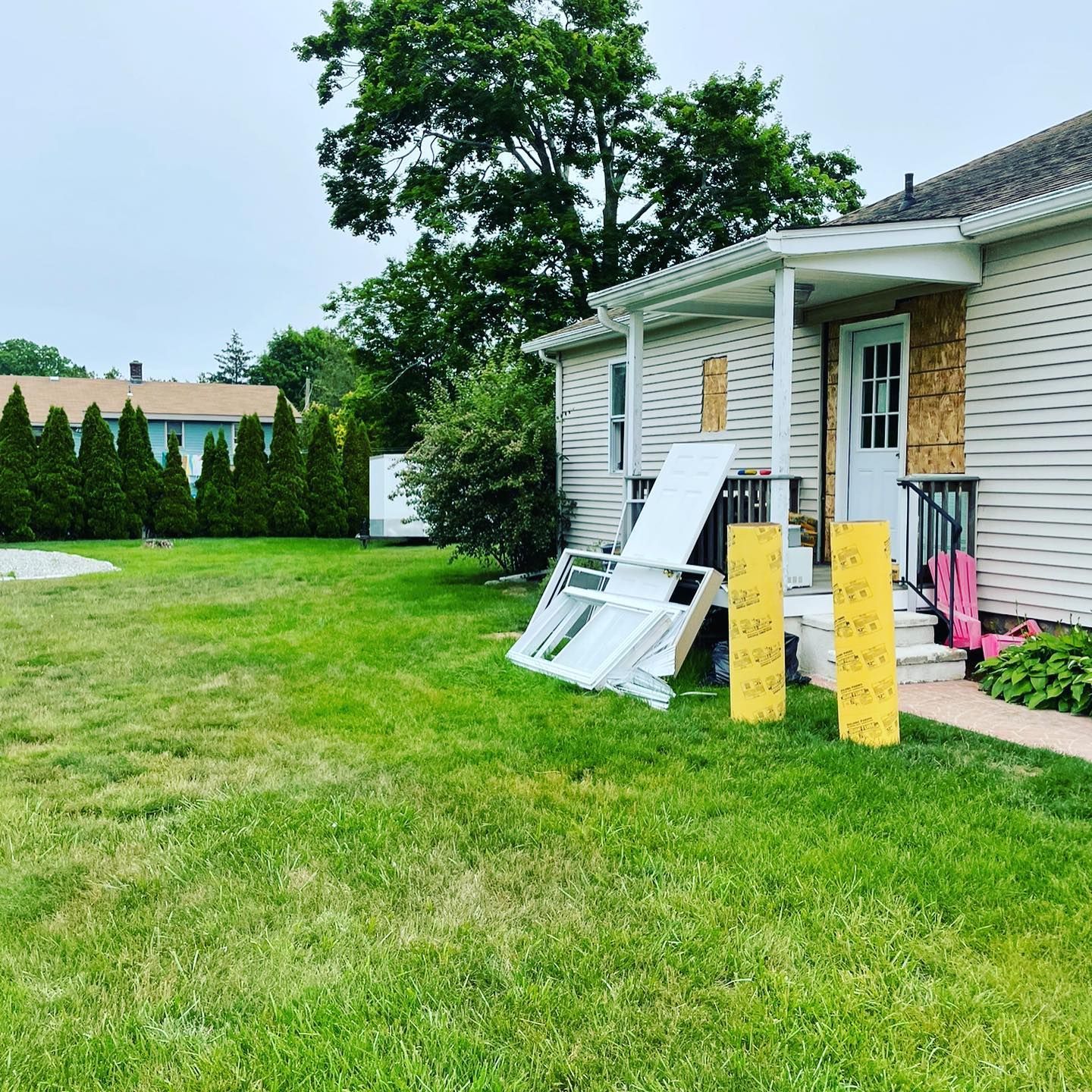 Lawn with house under renovation; siding removed near front door.  Debris and yellow signs are scattered on the grass.