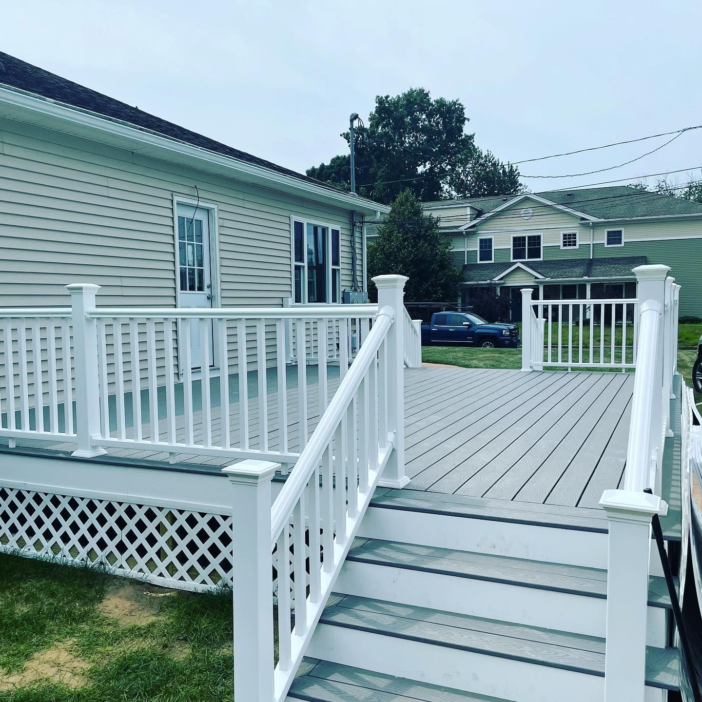 White-railed deck with gray flooring attached to a light-colored house. Steps lead down to a grassy lawn.