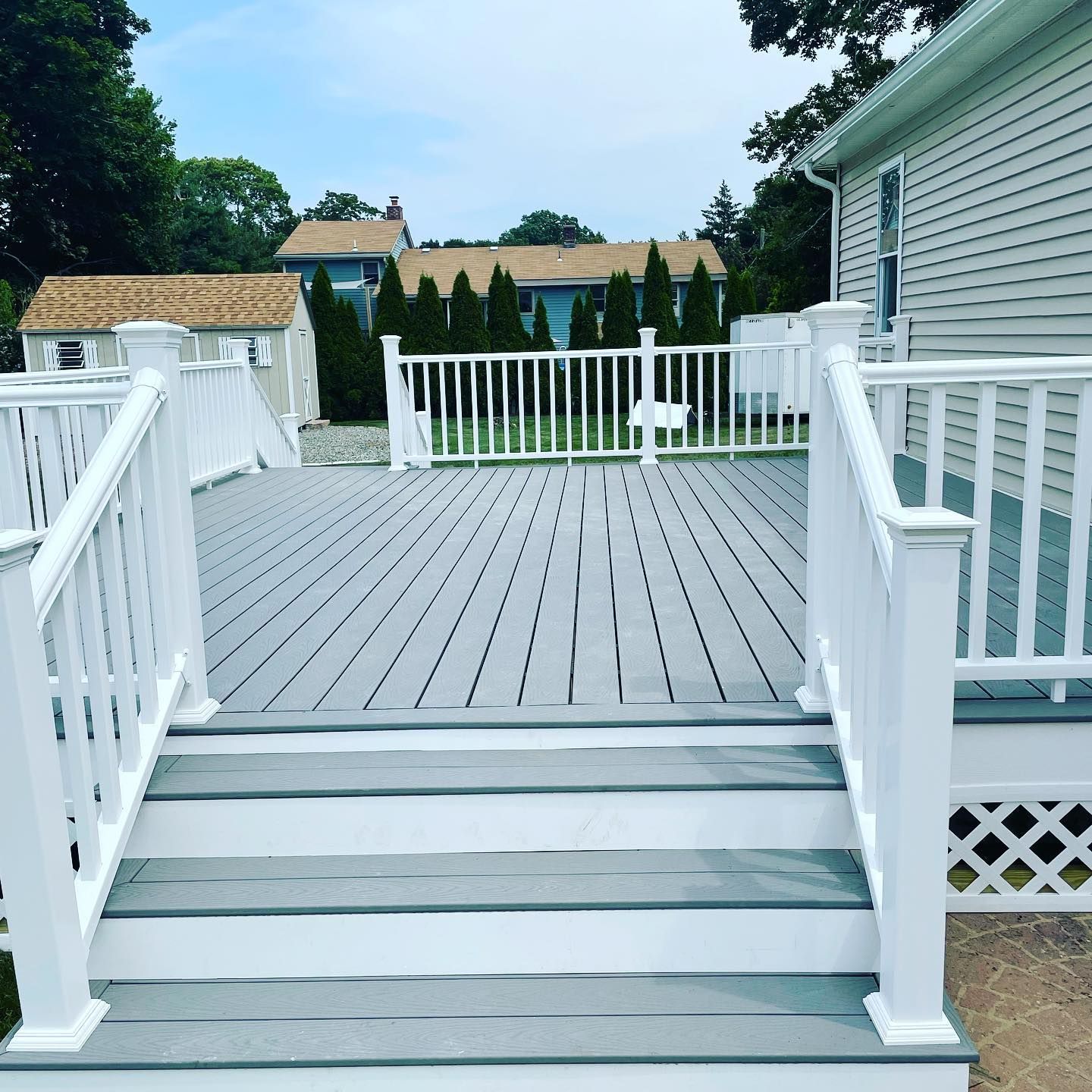 Gray deck with white railings and stairs, a house on the right, and other houses in the background.