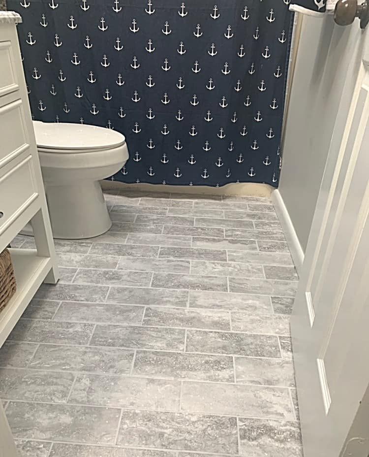 Bathroom with gray tile floor, white toilet, and nautical shower curtain with anchor pattern.