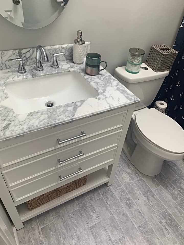 White bathroom vanity with marble top, sink, and toilet. Gray tile floor.