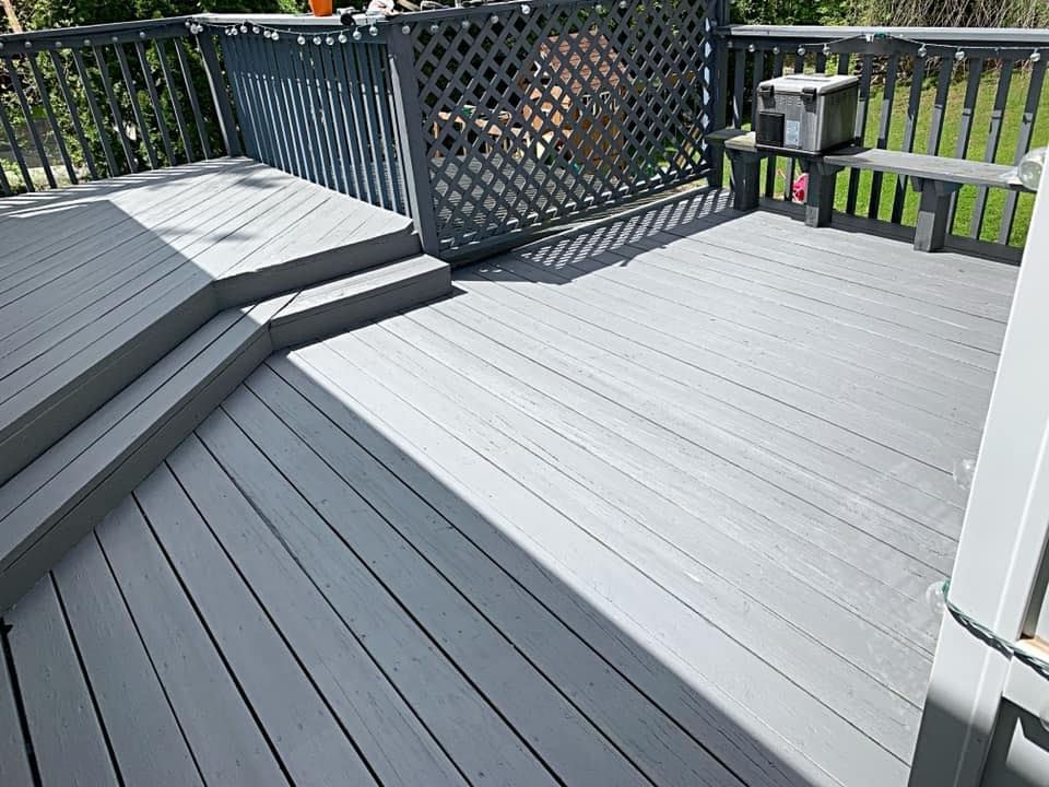 Gray wooden deck with built-in steps, lattice fence, and bench, in a sunlit outdoor setting.