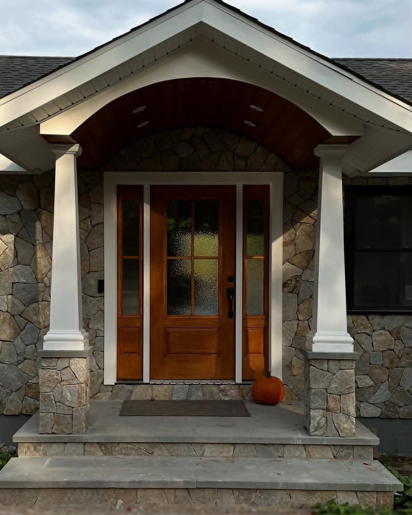 Entryway with stone walls, wooden door, and covered porch supported by white columns.