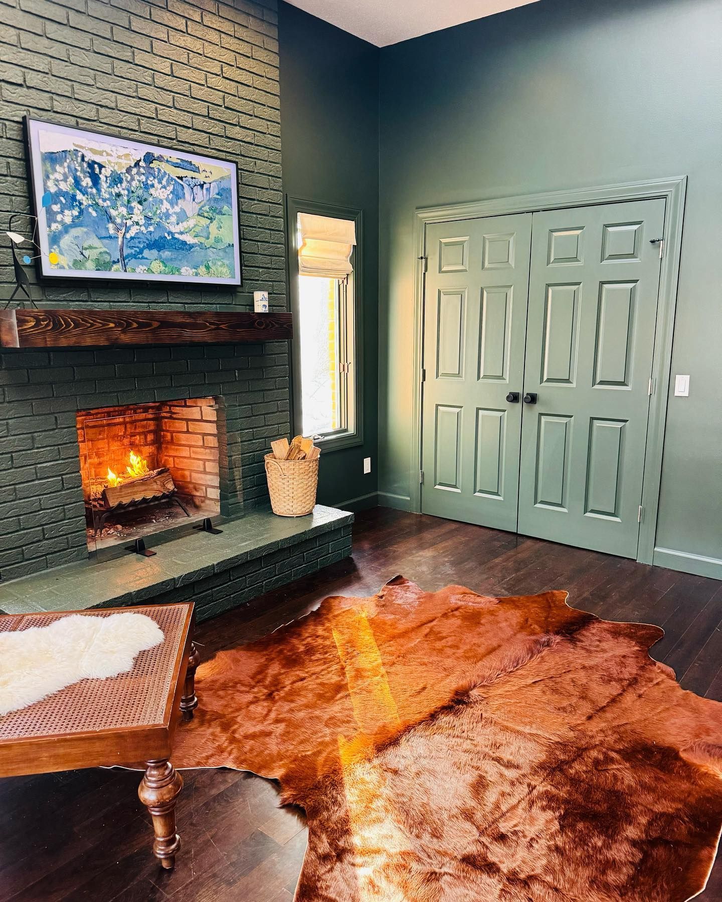 Cozy room with dark green walls, a fireplace, and a cowhide rug. A TV and closed doors are also present.