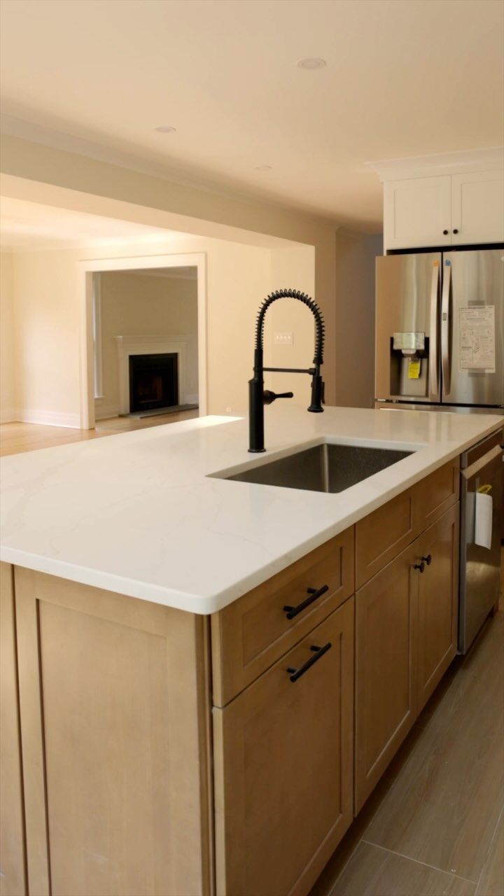 Kitchen island with sink, black faucet, light cabinets, light countertop, and stainless steel refrigerator.