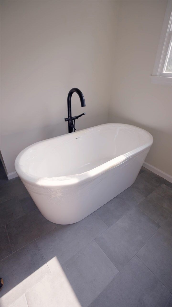 White oval bathtub with black faucet in a light-colored bathroom.