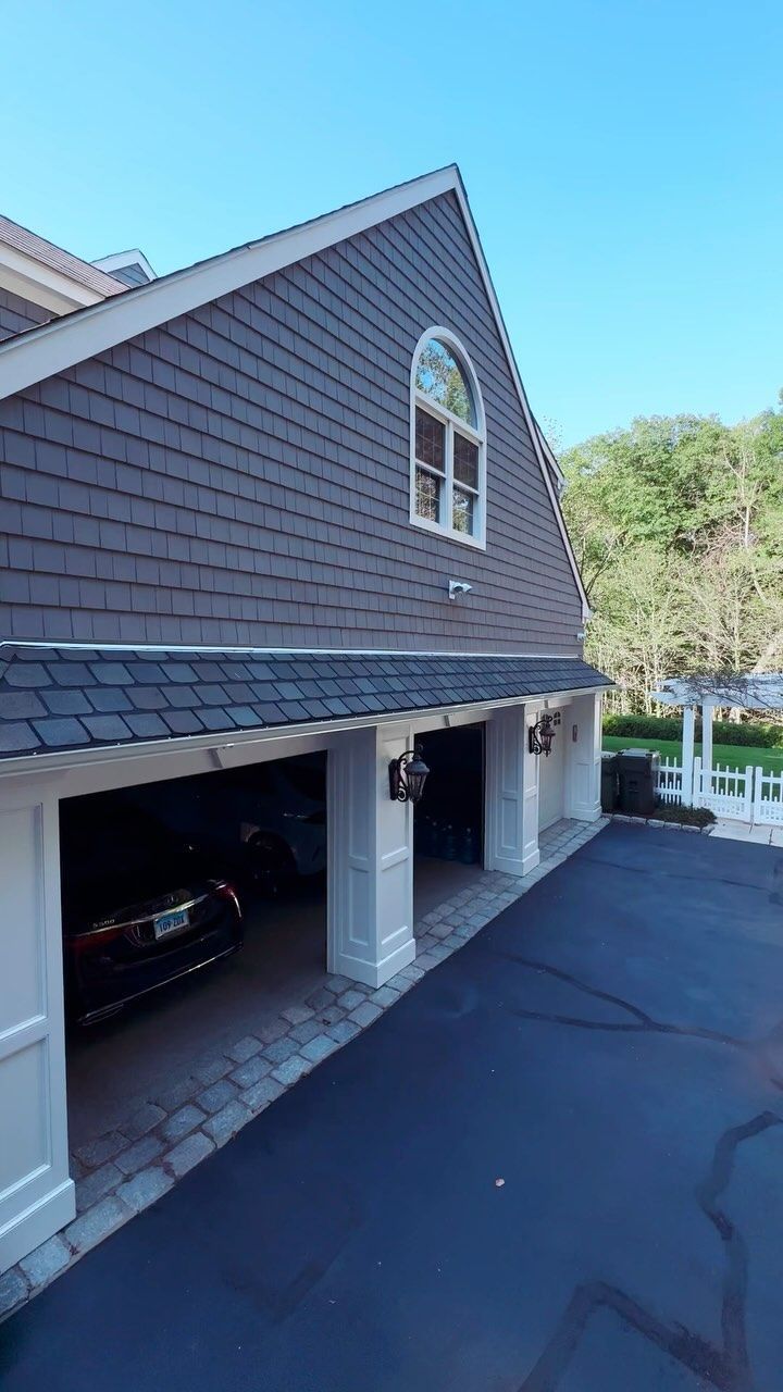 Three-car garage with dark asphalt driveway and gray shingle siding, under a clear blue sky.