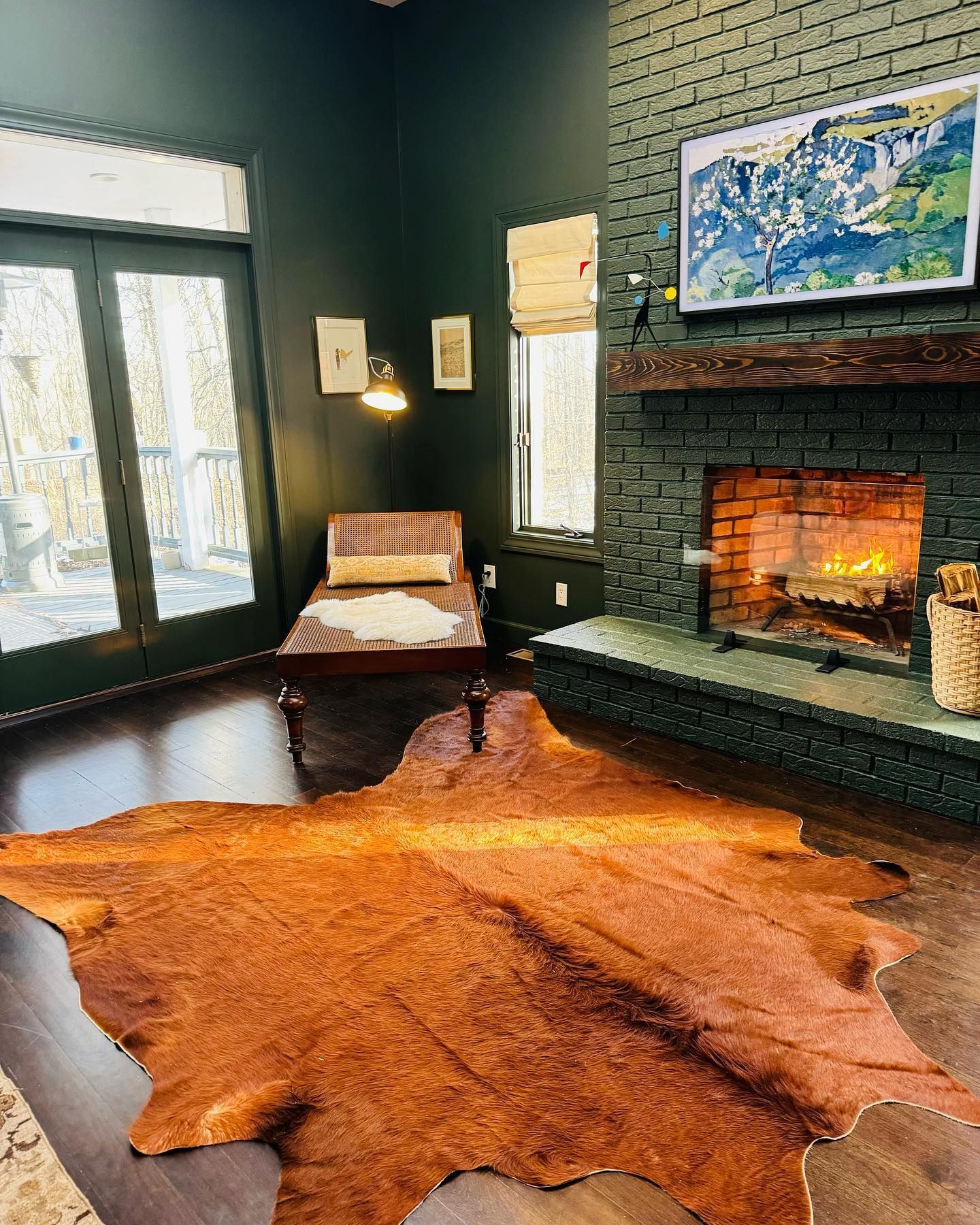 Cozy living room with dark green walls, fireplace, cowhide rug, and chaise lounge.