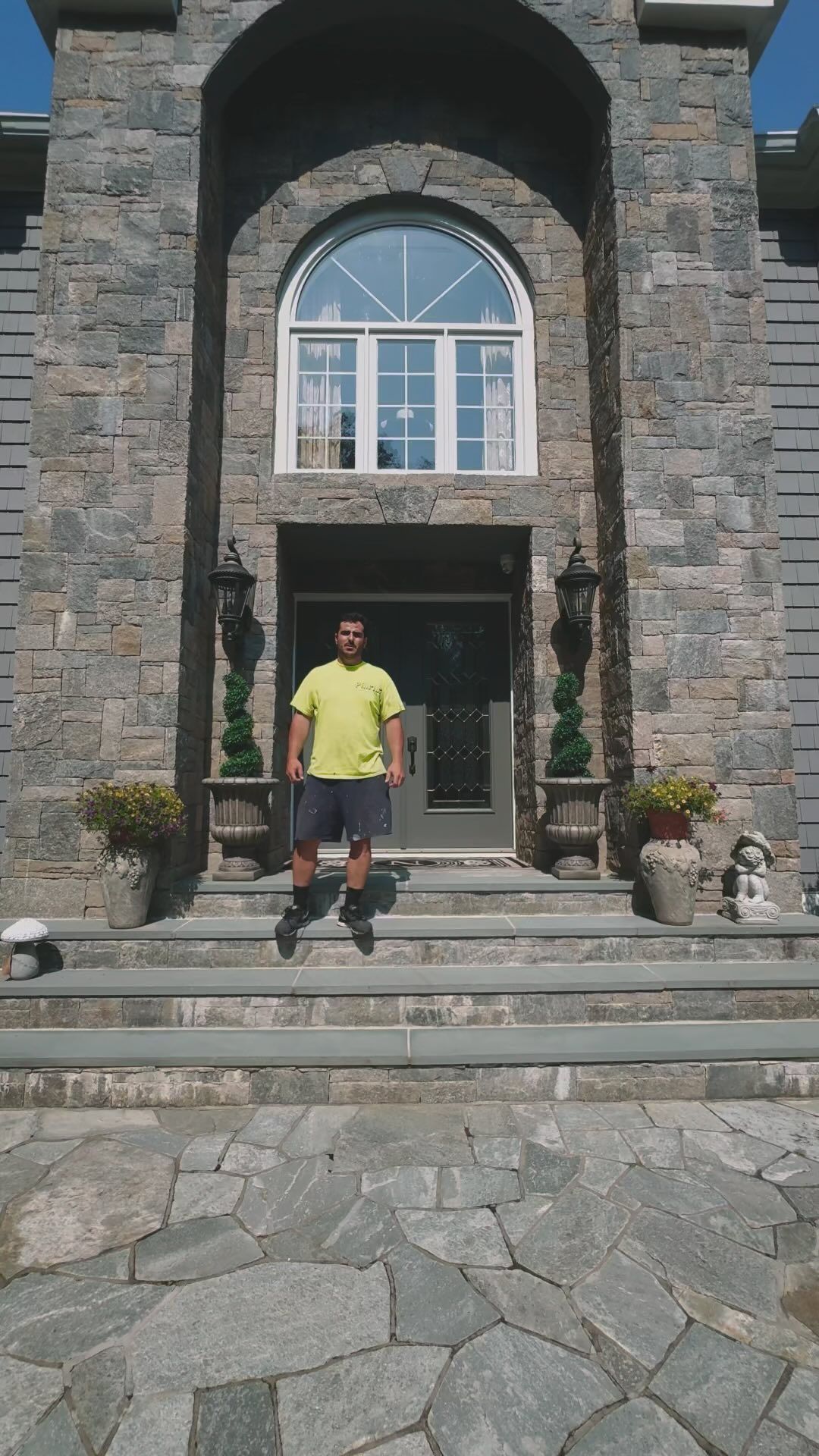 Man standing on steps in front of a stone house with an arched doorway.