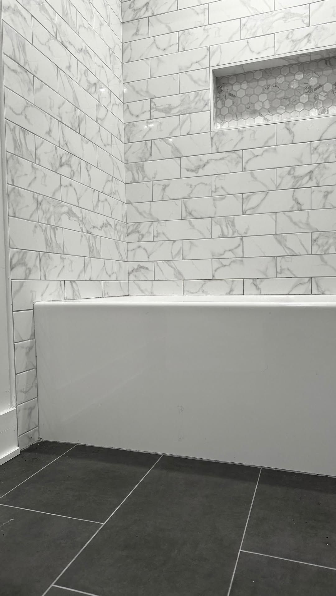 Bathroom with white and gray tiled walls, white bathtub, and dark gray tiled floor.