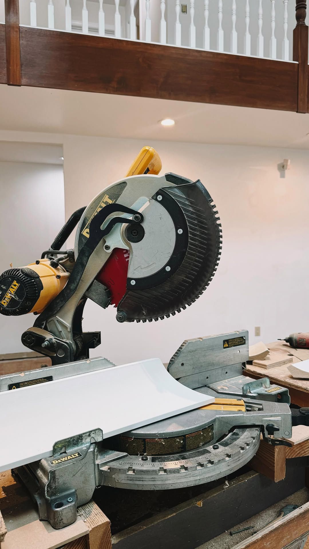 A miter saw cutting a white board, indoors. Yellow and silver saw, wood and white walls.