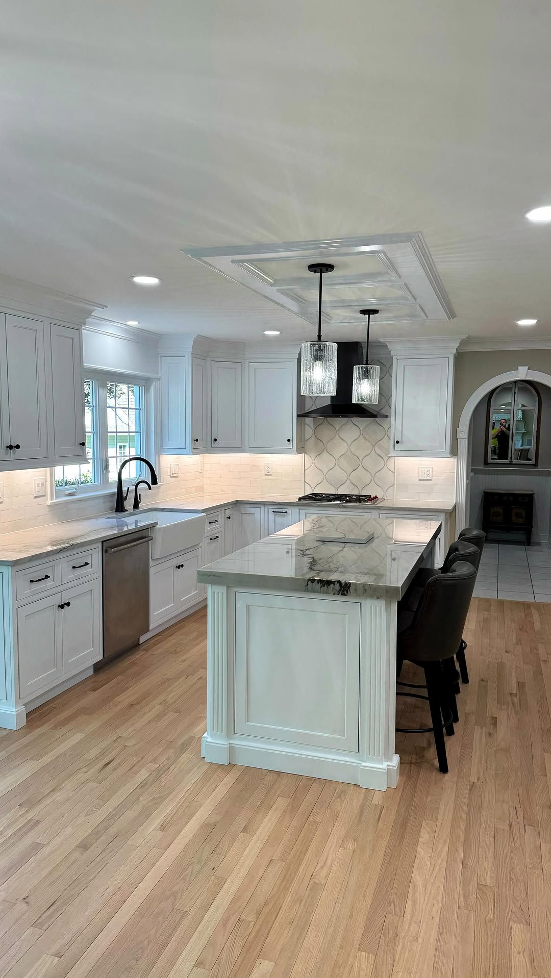 White kitchen with island and hardwood floors, overhead lights and fireplace.