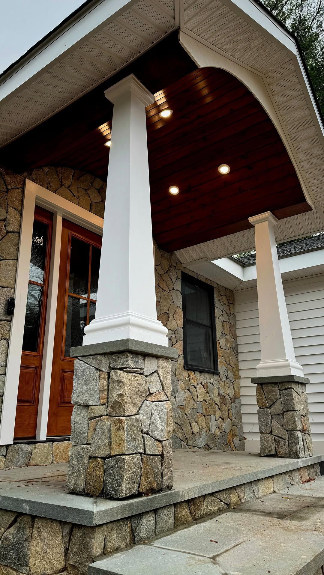 Stone facade with a covered porch supported by columns. White trim and wood door.