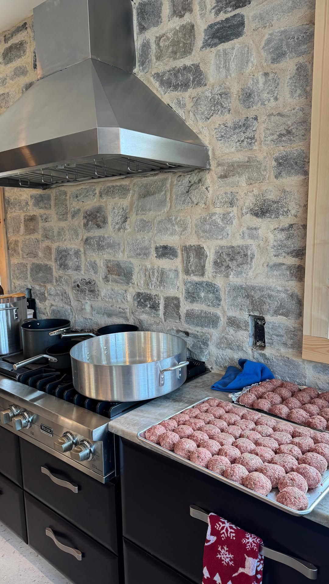 Kitchen scene: large pot on stove, a tray of raw meatballs, stainless steel vent hood and brick backsplash.
