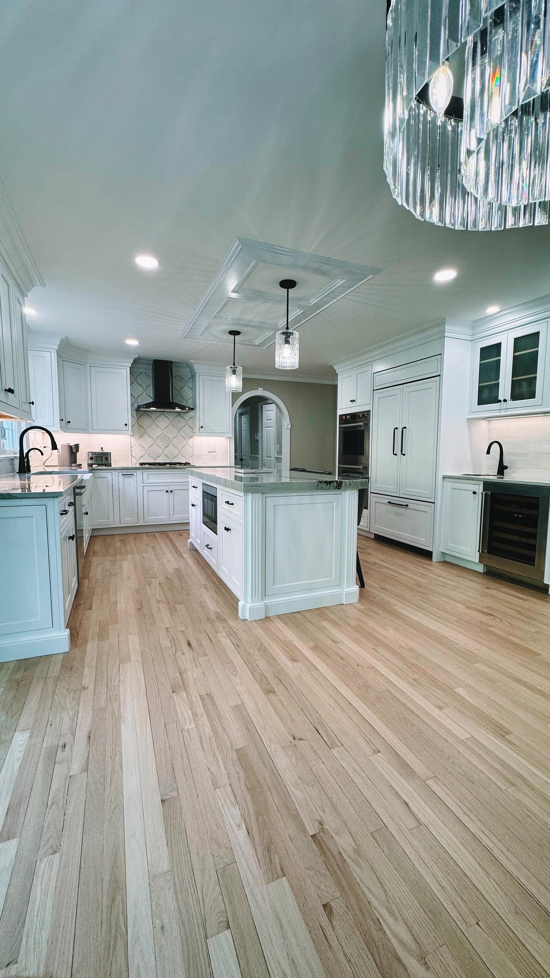 Spacious white kitchen with island, wood floors, and decorative lighting.