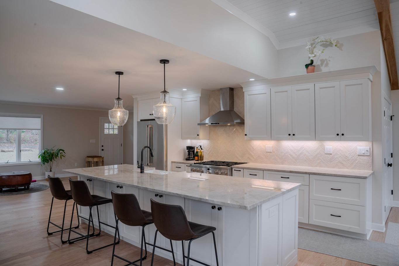 Modern white kitchen with island, stainless steel appliances, and bar stools.