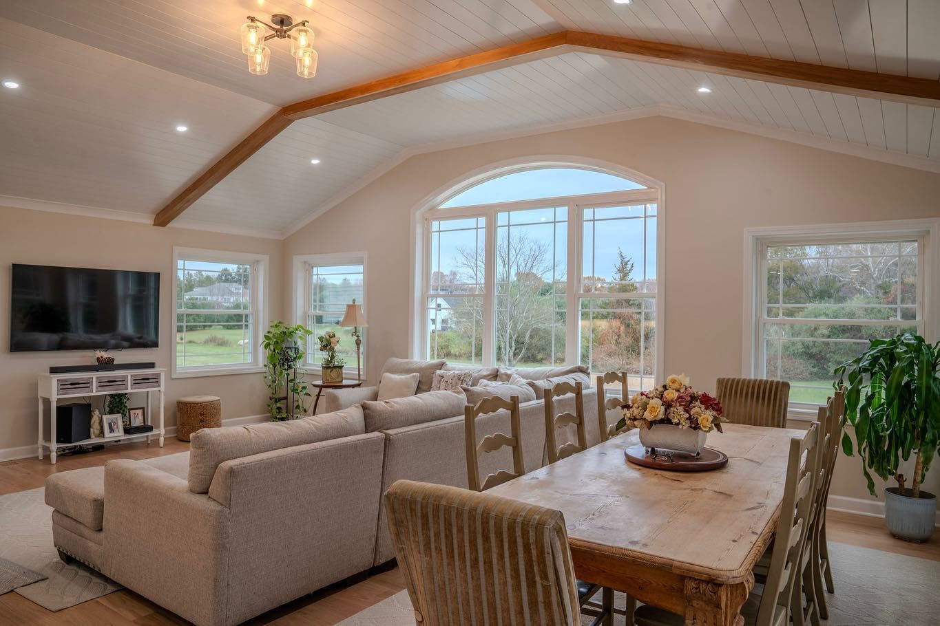 Spacious living room with large windows, light-colored walls, sofa, dining table, and natural light.