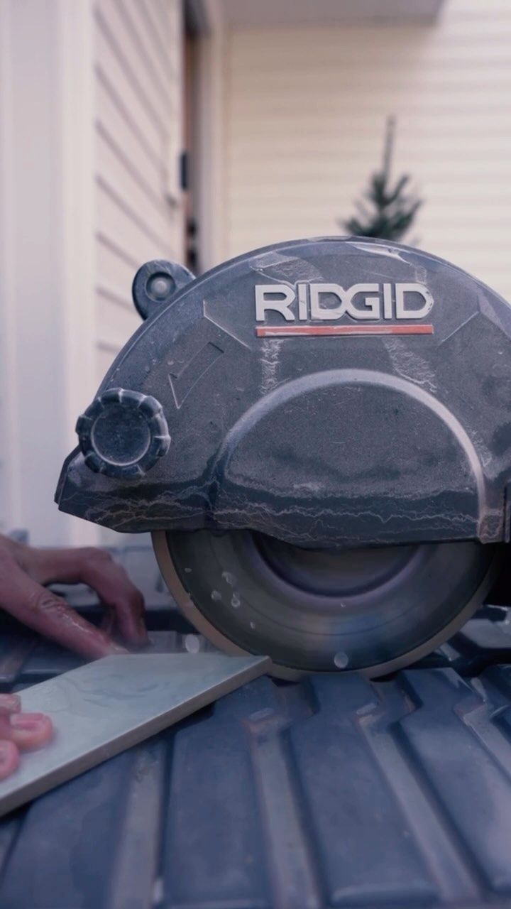 A person using a RIDGID tile saw to cut a ceramic tile outdoors.